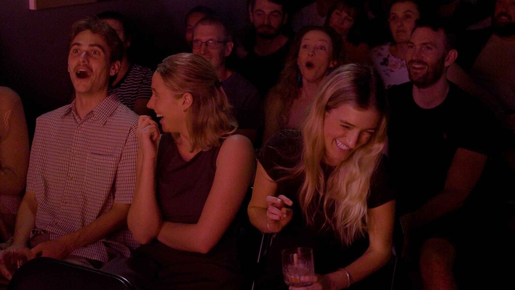 A group of people seated in a dimly lit room, likely attending an event or performance. 1