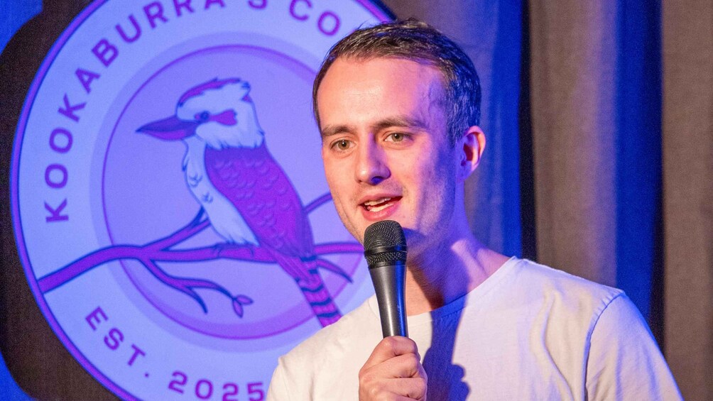 A person holding a microphone with a logo featuring a bird and text 'Kookaburra Co. EST. 2025' in the background. 4