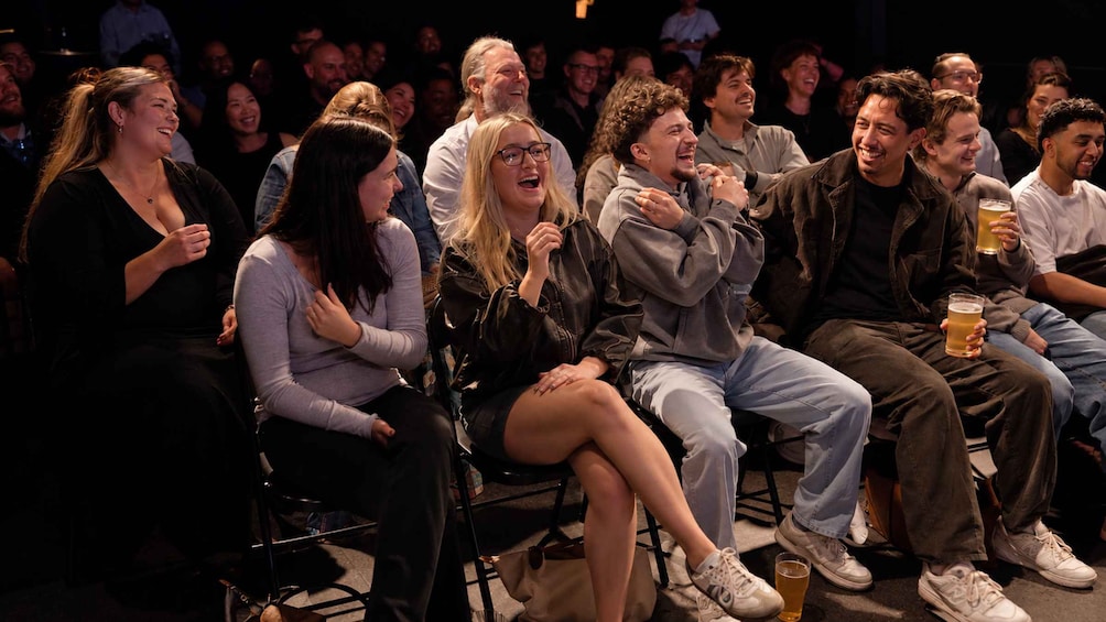 A group of people seated in an auditorium, some holding drinks. 5