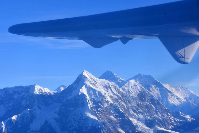 A mountain range with snow-capped peaks and an airplane wing in the foreground. 2