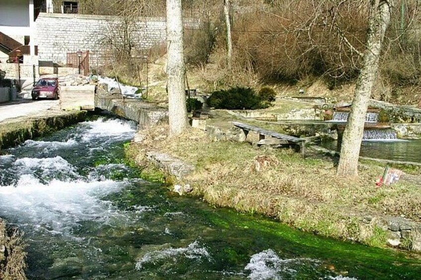 A river with a bridge, benches, and trees. 2