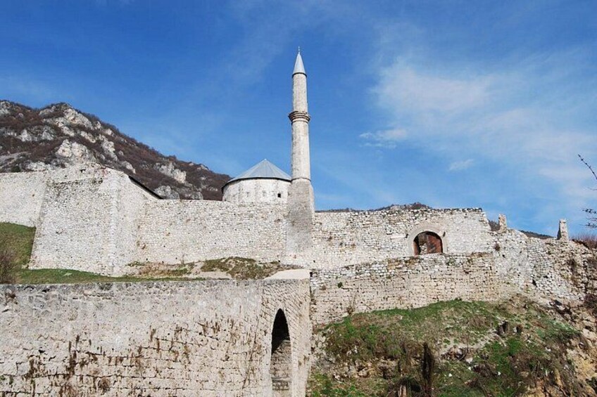 A historic stone fortress with a prominent minaret, surrounded by rugged terrain and a clear sky. 3