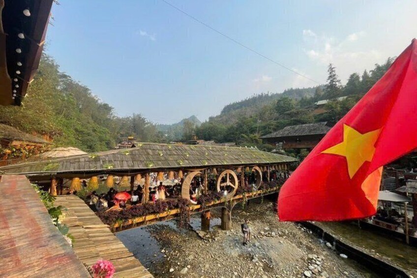 A wooden bridge over a river with a red flag featuring a yellow star. 3