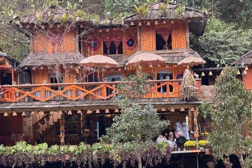 A multi-story wooden house with balconies, surrounded by lush greenery. 1
