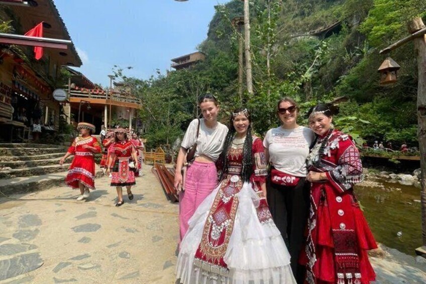 A group of people in traditional attire on a stone bridge with a river and greenery in the background. 4