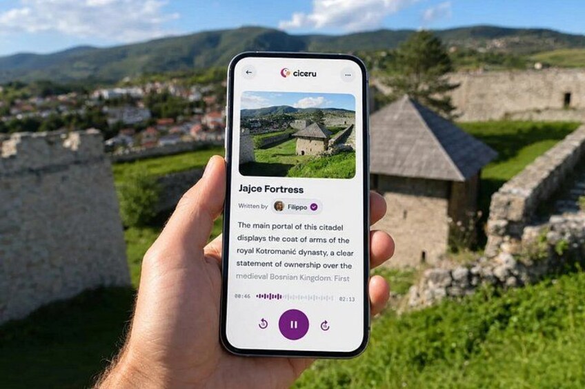 A hand holding a smartphone displaying a photo of Jaje Fortress with a description. 1