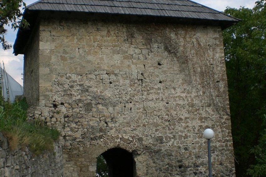 A weathered stone building with a small arched entrance and a metal roof. 5
