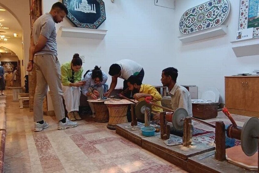 A group of people engaged in a traditional activity, possibly weaving or crafting, in a room with patterned rugs and wooden furniture. 5