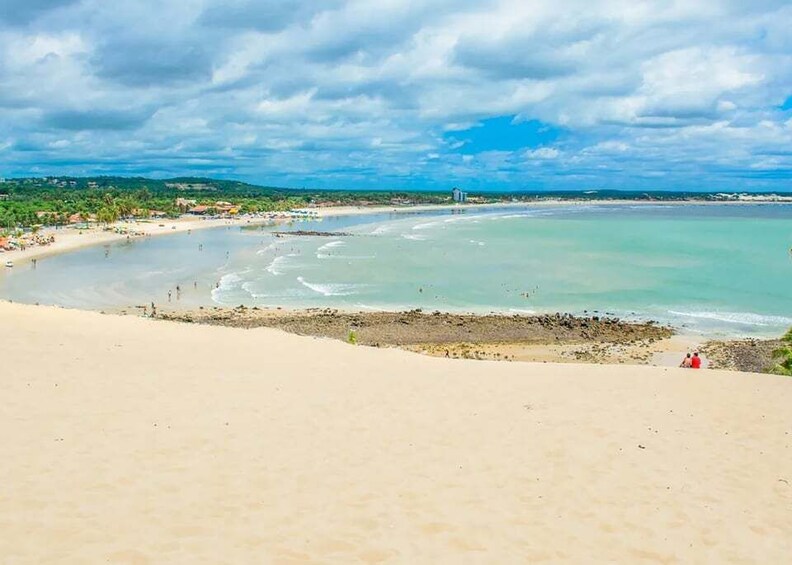A beach with clear turquoise waters, a sandy shore, and a distant view of a city skyline. 2