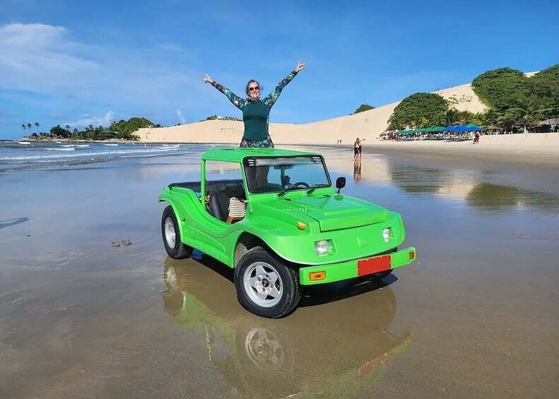 A green car on a beach with a person standing on top. 3