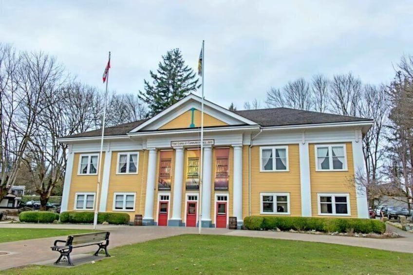A yellow building with a red door, a flag, and a bench in front. 3