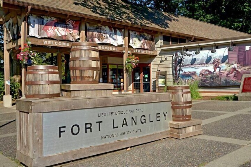 A wooden sign with 'FORT LANGLEY NATIONAL HISTORIC SITE' and a building with 'WELCOME' banners. 1
