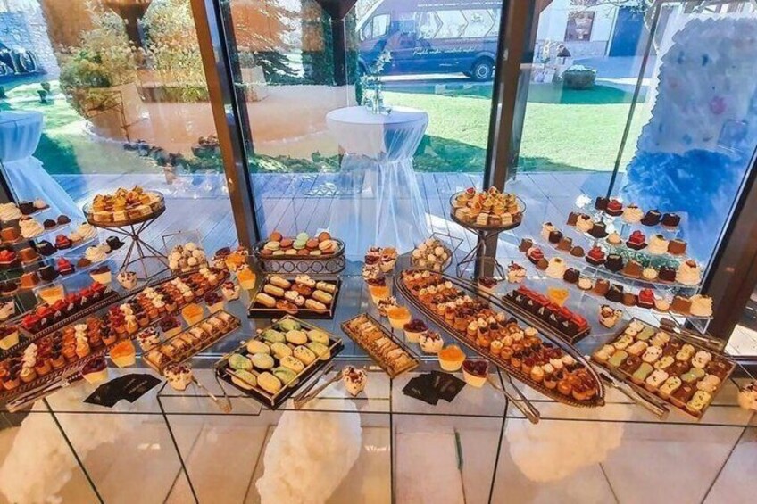 A variety of pastries and desserts displayed on trays and stands inside a building with large windows. 4