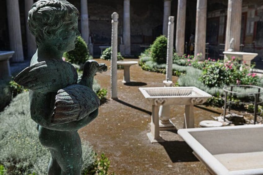 A statue of a cherub holding a bird in a garden with classical columns and a fountain. 4