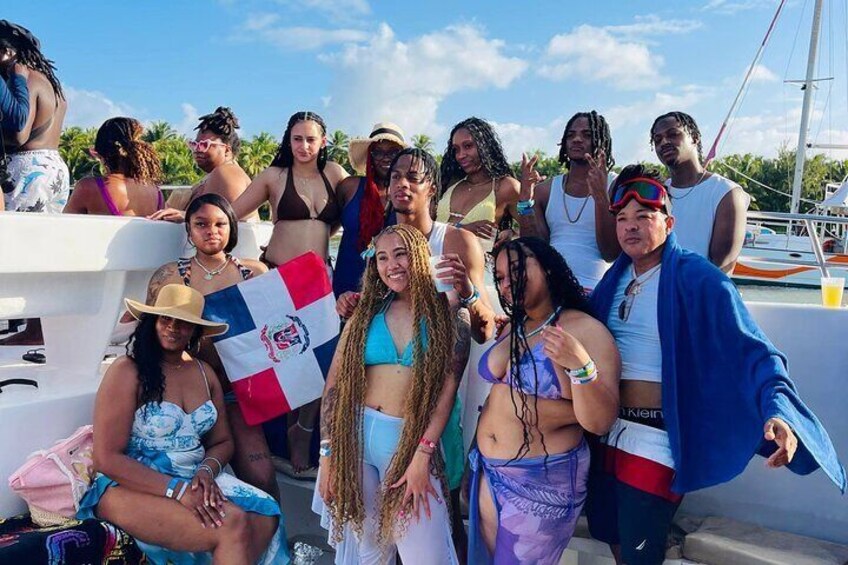 A group of people on a boat with a flag, tropical vegetation, and a clear sky. 5