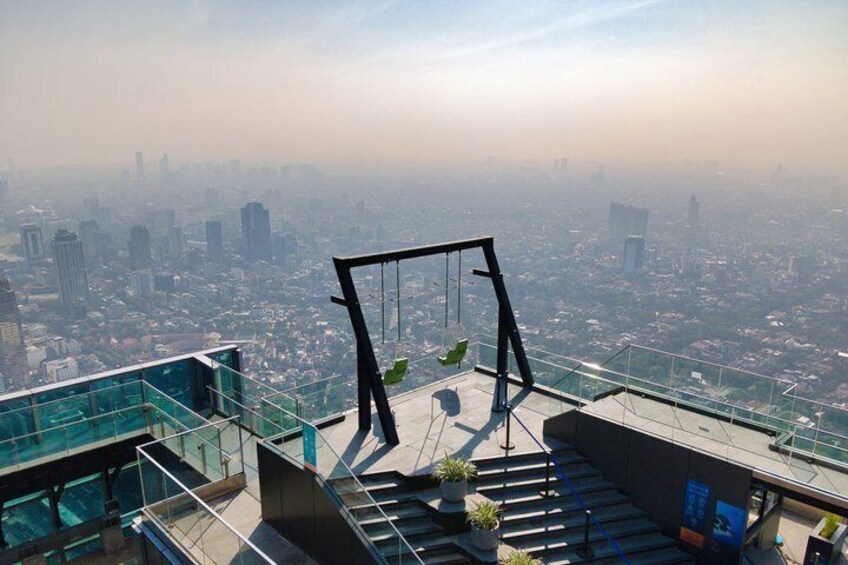 A high-rise building with a glass railing, a swing set, and a cityscape in the background. 5