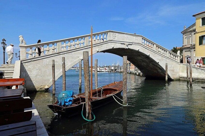A stone bridge over water, wooden boats, and a statue. 3