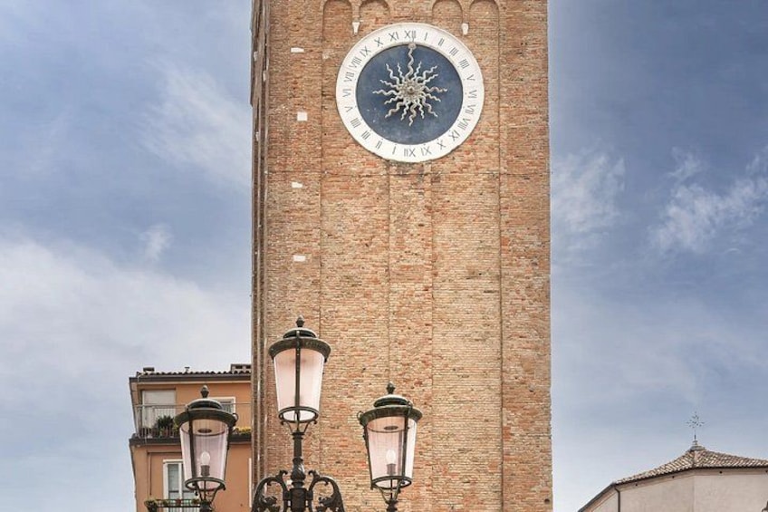 A tall brick tower with a large clock face and two street lamps. 5