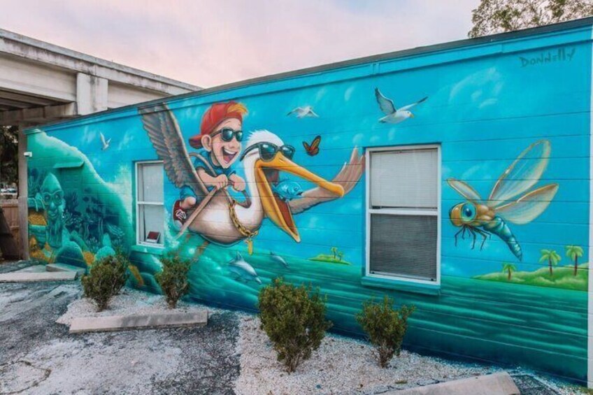 A mural on a building featuring a character with a bird, a dragonfly, and a seagull. 3