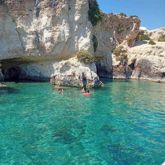 A clear turquoise sea with rocky cliffs and a person swimming. 5