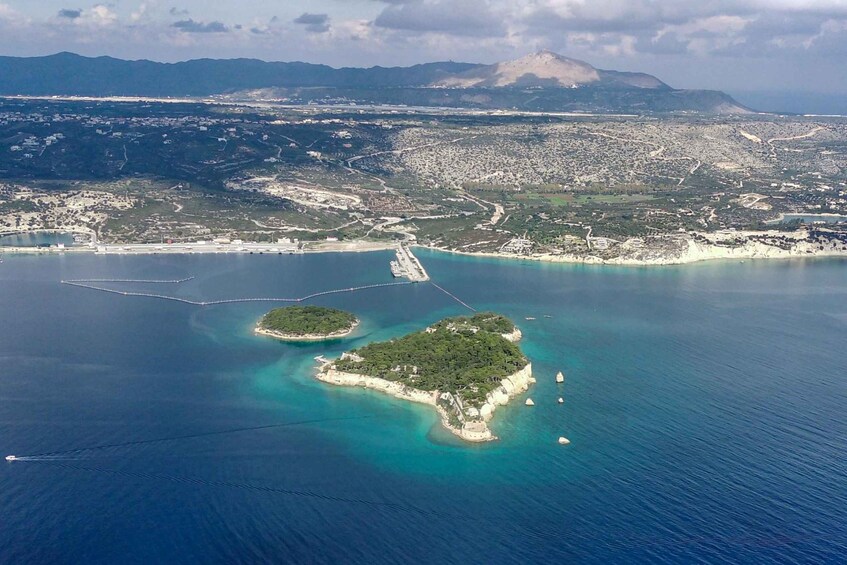 An aerial view of a coastal city with a prominent island, clear blue waters, and distant mountains. 2