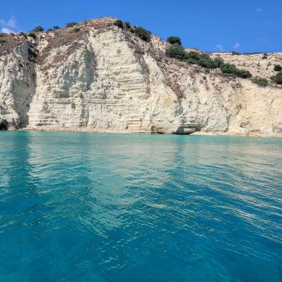 A coastal cliff with layered sedimentary rock formations and clear turquoise water. 4