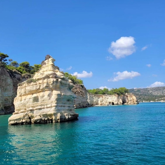 A coastal rock formation with clear blue waters and distant hills. 1