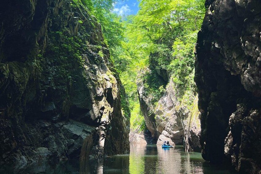 A narrow waterway flanked by rocky cliffs, a person paddling a kayak, and dense green foliage. 5