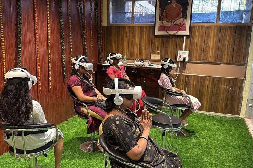 A room with four people wearing VR headsets seated on chairs, a wooden wall, and a poster. 2