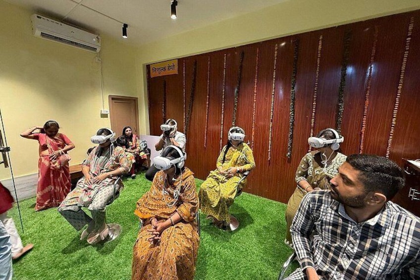 A group of people sitting on green carpet, wearing VR headsets, in a room with wooden paneling and a sign in a foreign language. 2