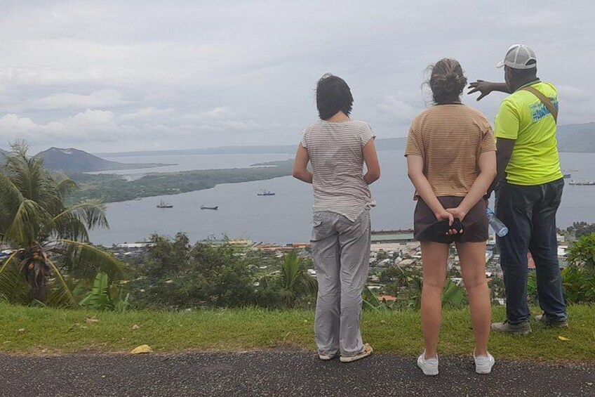 Three people standing on a road overlooking a body of water with ships. 2