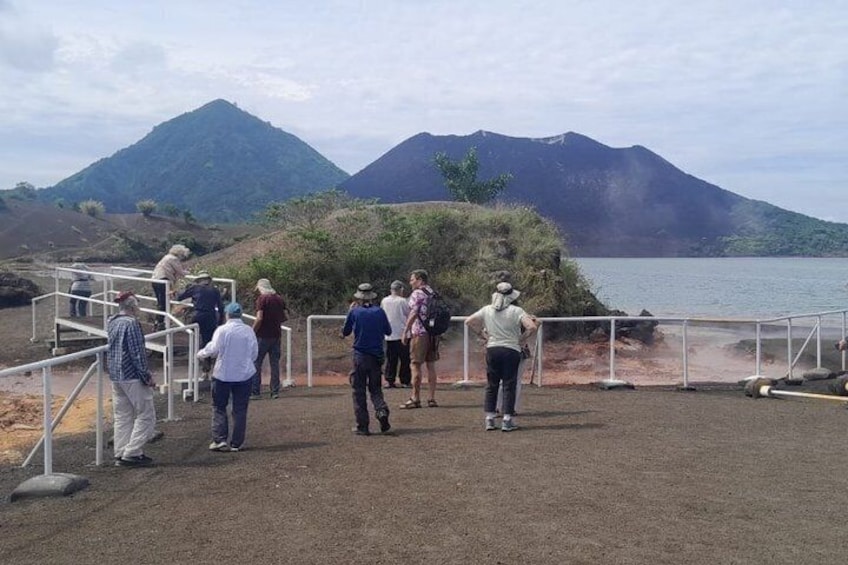A group of people standing near a railing overlooking a body of water with mountains in the background. 2