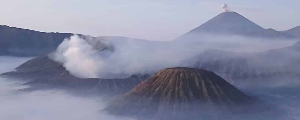 A volcanic landscape with active fumaroles and a smoke plume. 5