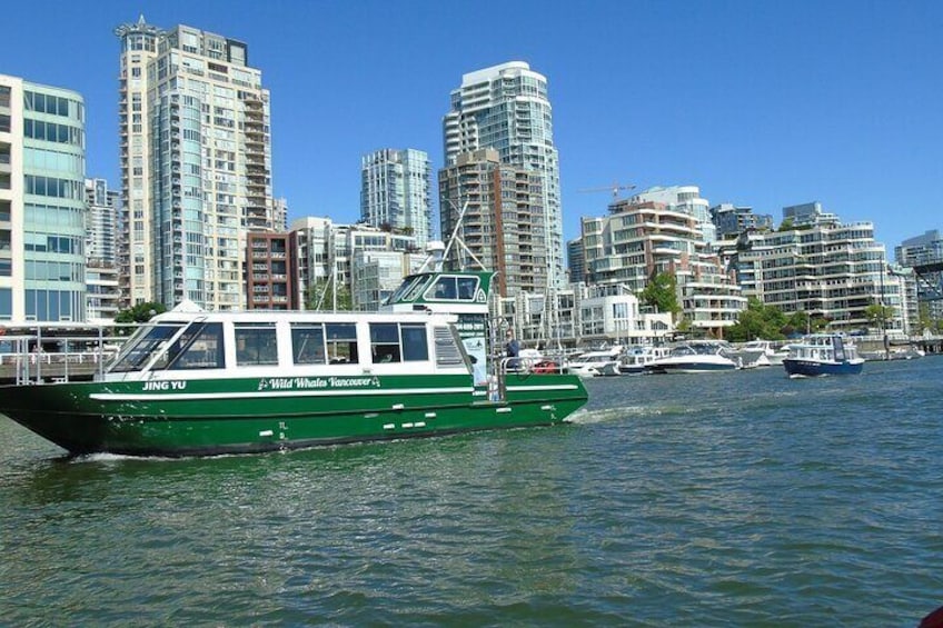 A green boat with 'JING YU' written on it, a city skyline in the background, and a clear blue sky. 2