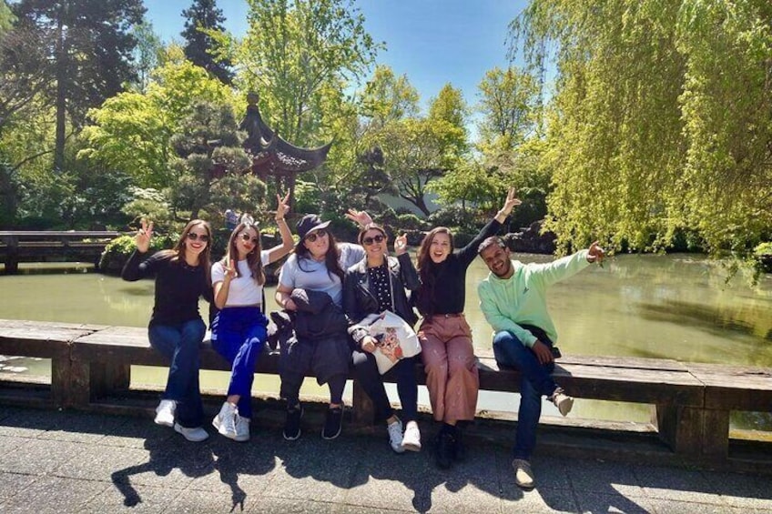 A group of people sitting on a bench by a pond with trees in the background. 1