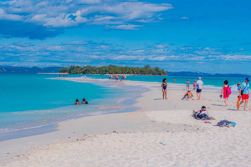 A beach with people sunbathing and swimming, clear turquoise water, and a distant island. 4
