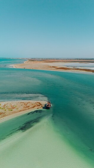 An aerial view of a coastal area with clear turquoise waters, a sandy beach, and a ship anchored near the shore. 5