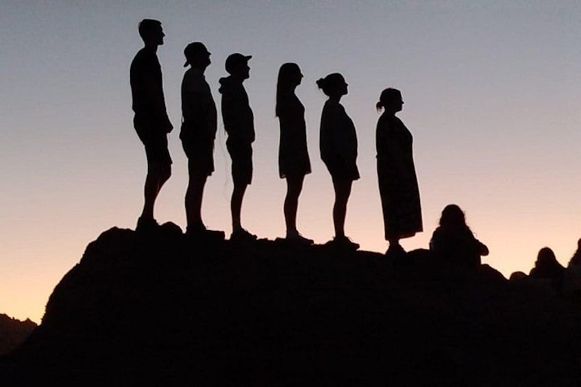 Silhouettes of people standing on a rocky outcrop against a sunset sky. 4