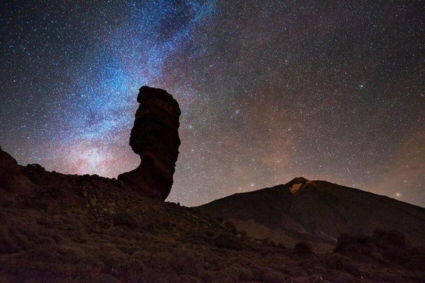 A starry night sky with a prominent rock formation silhouetted against it. 1