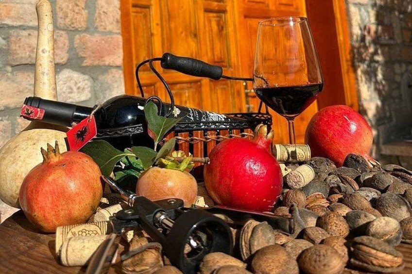 A table with a wine bottle, wine glass, pomegranates, nuts, and a corkscrew. 5