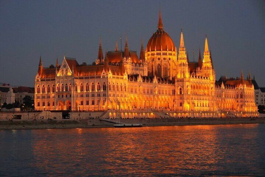 A grand, illuminated building with multiple spires and domes, reflecting on the water. 1