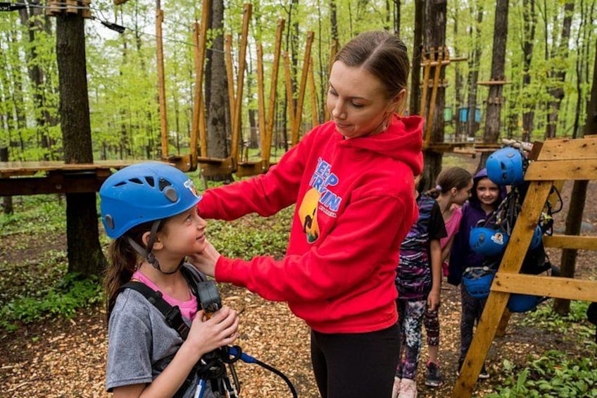 An instructor assisting a child with a helmet in a forested area with wooden structures. 3