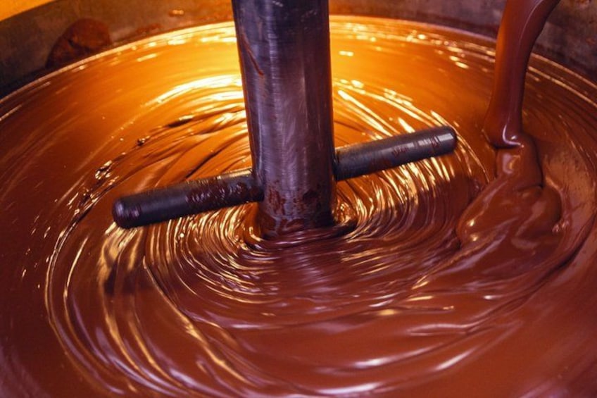 A large vat of chocolate being stirred with a mechanical arm. 3