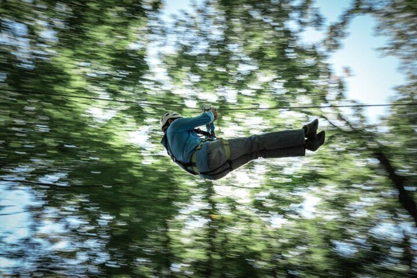 A person suspended in mid-air, wearing a helmet and harness, with trees in the background. 4
