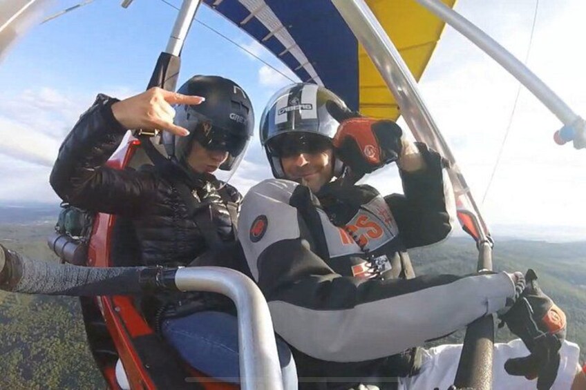 Two people in a tandem hang glider with a mountainous landscape in the background. 2