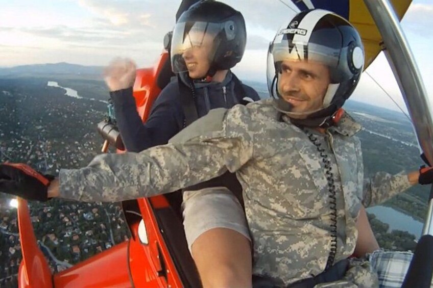 Two individuals in military flight gear on a helicopter, with a landscape view below. 3