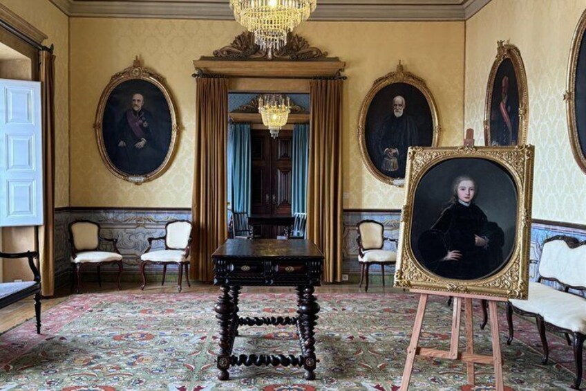 An ornate room with a chandelier, a portrait on an easel, and a large table. 3