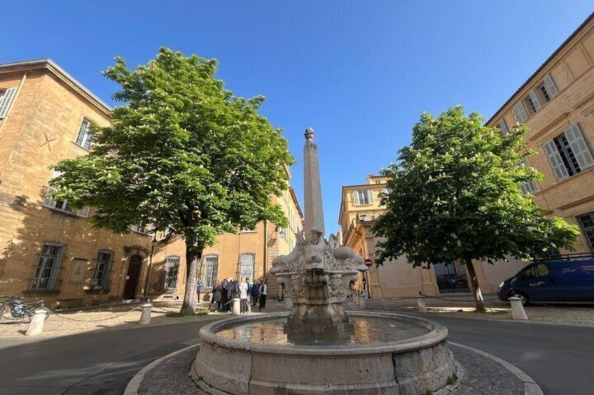 A fountain with a statue in the center, surrounded by trees and historic buildings. 2