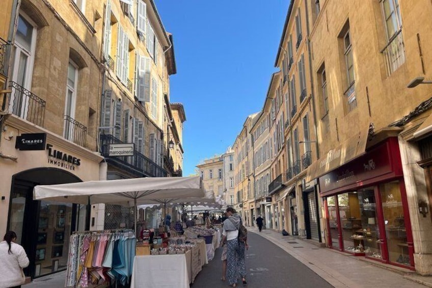 A street with a market stall selling textiles, a clothing store, and a jewelry shop. 4