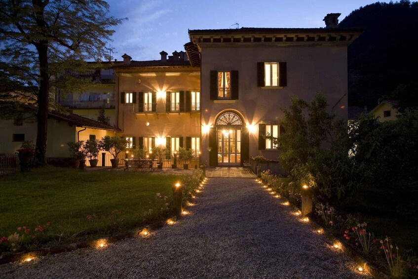 A two-story building with a gravel pathway leading to the entrance, surrounded by a garden with lights. 1